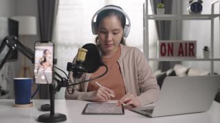一名年轻的亚洲女子用耳机和麦克风录制播客，看着镜头说话视频素材模板下载