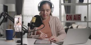 一名年轻的亚洲女子用耳机和麦克风录制播客，看着镜头说话
