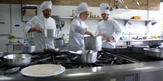 拉丁美洲女厨师准备意大利面菜与男副厨师在一家餐馆