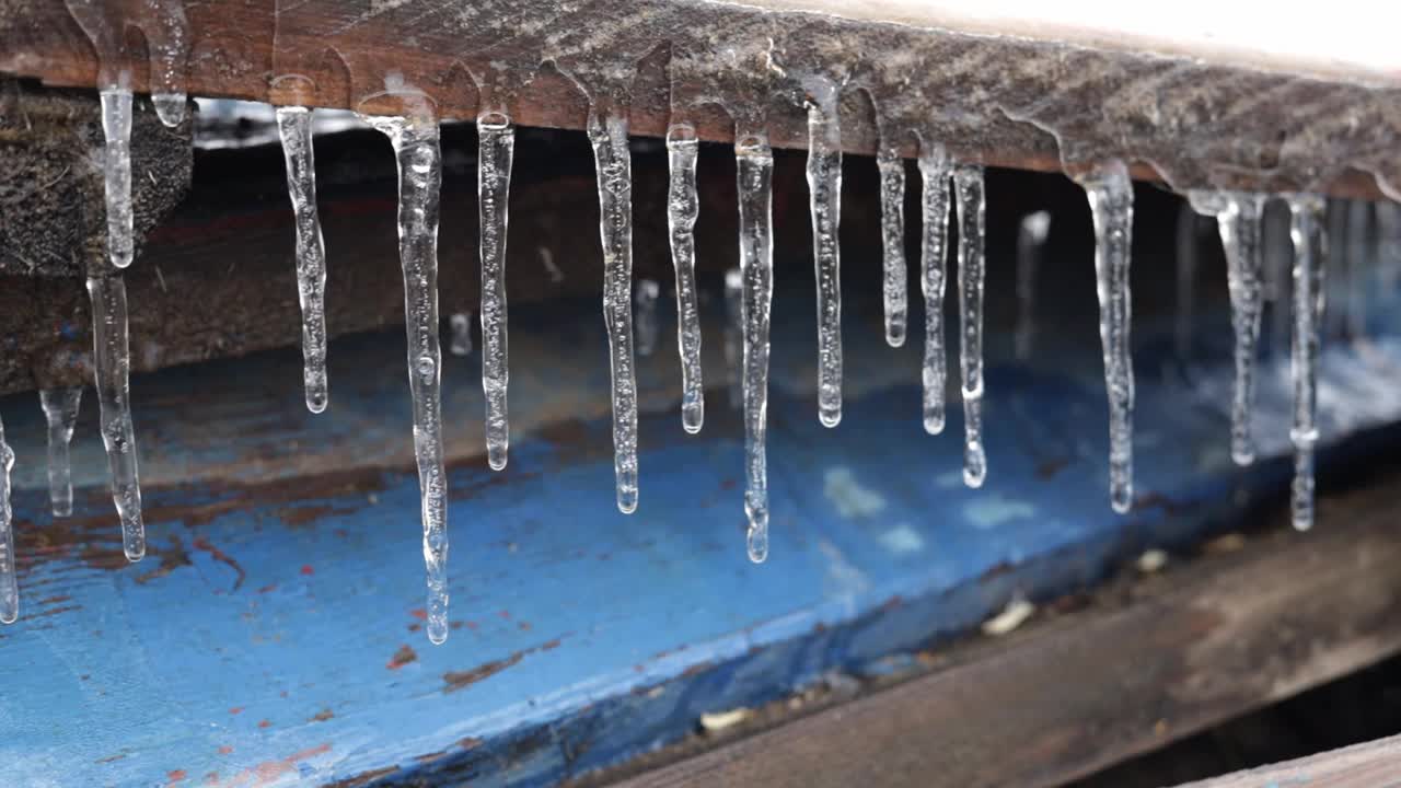冰柱悬挂在木板上和水滴上。第一次霜冻。气候变化的概念。春天的时间