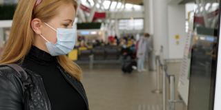 一名戴着医用口罩的妇女在机场触摸敏感屏幕。