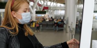 一名戴着医用口罩的妇女在机场触摸敏感屏幕。