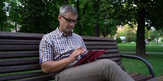 一名戴眼镜的男子在城市公园的平板电脑上浏览社交媒体