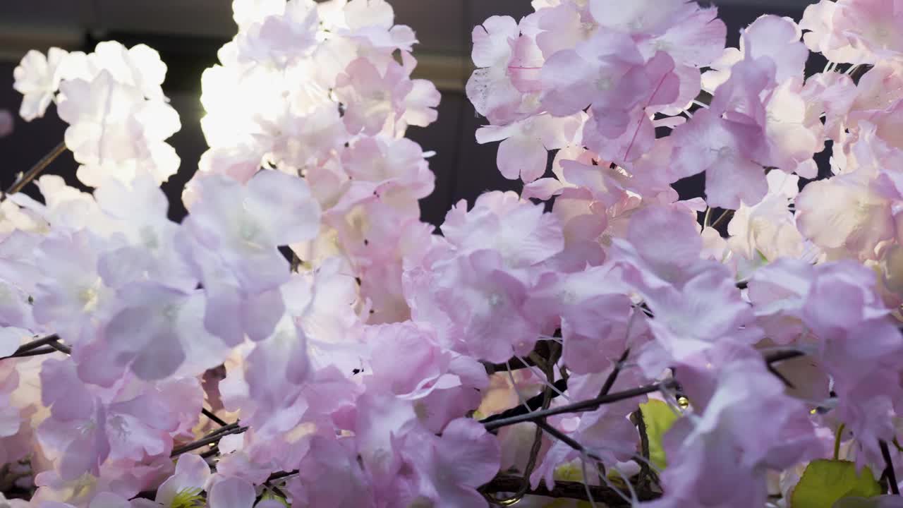 近距离观察树上的粉色塑料花。树上有很多小LED灯泡。卡车从右向左射击。上面有一个聚光灯。