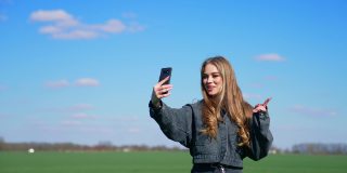 年轻的女博主使用电话在外地。迷人的女孩领导她的博客页面通过手机在自然的背景。