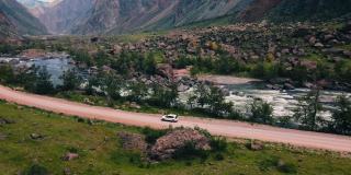 一辆白色的越野车正沿着巨大的卡图-亚历克峡谷(Katu-Yaryk canyon Chulyshman Valley)的一条空旷的乡村公路行驶。阿尔泰、西伯利亚,俄罗斯