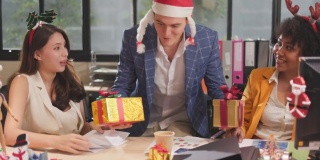 年轻的商务团队在办公室里庆祝节日，都戴着圣诞老人的帽子，给同事送礼物。办公室里相爱的漂亮年轻人，交换礼物盒庆祝。
