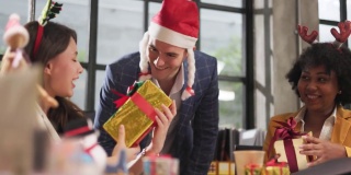 年轻的商务团队在办公室里庆祝节日，都戴着圣诞老人的帽子，给同事送礼物。办公室里相爱的漂亮年轻人，交换礼物盒庆祝。