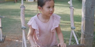 手持式慢动作快乐的年轻混合亚洲女孩笑微笑和有乐趣的秋千在操场，夏季户外公园