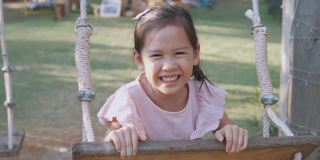 手持式慢动作快乐的年轻混合亚洲女孩笑微笑和有乐趣的秋千在操场，夏季户外公园
