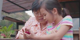 亚洲孙女教奶奶使用智能手机，帮助银发一代使用数字技术，社交距离家庭，多代概念