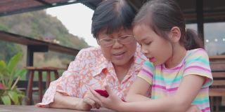 亚洲孙女教奶奶使用智能手机，帮助银发一代使用数字技术，社交距离家庭，多代概念