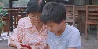 亚洲孙子教奶奶使用智能手机，帮助银发一代使用数字技术，社交距离家庭，多代概念