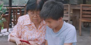 亚洲孙子教奶奶使用智能手机，帮助银发一代使用数字技术，社交距离家庭，多代概念