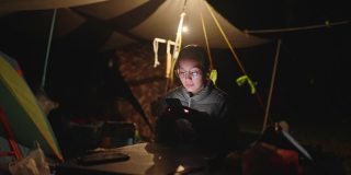 亚洲妇女晚上在帐篷里露营时使用手机