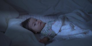 疲倦的亚洲婴儿婴儿揉眼睛由于过敏，当睡觉在床上。尘螨过敏。