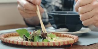 在一家亚洲餐馆里，一名男子用筷子吃生菜叶子