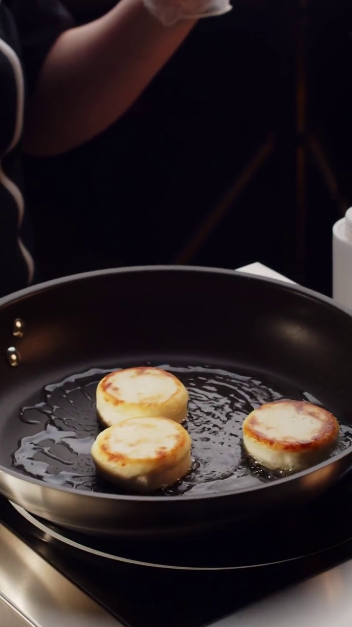 近距离拍摄金黄的松软干酪在煎锅中旋转煎炸。俄罗斯，乌克兰，白俄罗斯的美食。准备健康美味的早餐奶酪蛋糕