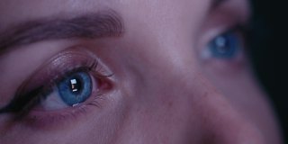 极度近距离的美丽女人的蓝色眼睛沉迷于社交网络，看着一个智能手机屏幕与快速闪烁的社交网络feed，帖子。闪烁的屏幕反射在眼睛里