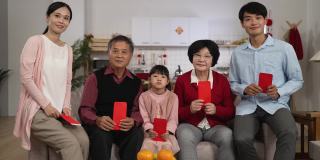 春节期间，幸福的五代家庭在家里拿着红包，对着镜头微笑，用拇指和胜利的手势拍照
