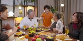 幸福亚洲多代人一起用餐，一家人手牵手祈祷感恩节前的节日晚餐，祖父母孙辈们一起呆在感恩节的传统晚餐家中