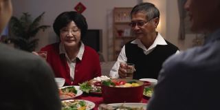 一位身着红色衣服的快乐老妇人在家中举行的团圆饭会上举起酒杯，向家人敬酒，庆贺农历新年