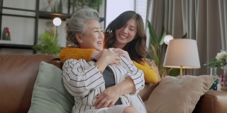 幸福的亚洲家庭偷拍的女儿拥抱祖父母妈妈年长的年长的妈妈舒适地放松在客厅的沙发沙发上，美丽的家庭的母亲和女儿在一起，拥抱和亲吻在家里