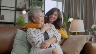 幸福的亚洲家庭偷拍的女儿拥抱祖父母妈妈年长的年长的妈妈舒适地放松在客厅的沙发沙发上，美丽的家庭的母亲和女儿在一起，拥抱和亲吻在家里视频素材模板下载