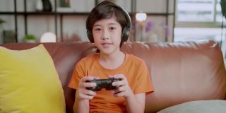 亚洲男孩流媒体游戏在线沉迷于智能手机游戏手机戴耳机，退出了亚洲男孩手玩智能手机游戏在线通过互联网在家里的沙发上，呆在家里的想法概念
