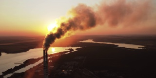 太阳下山后，管道产生的烟尘污染了大气。生态污染。夕阳下的湖泊背景上，工业烟囱排放出的烟尘。