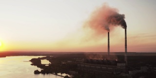 黄昏时河边的有害工厂。夕阳西下时，烟囱向空中喷出黑烟的工业区。环境污染。鸟瞰图。