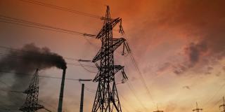 工厂烟囱附近的电力塔冒着黑烟。输电线路在夕阳下从管道中释放出有害气体。环境污染。