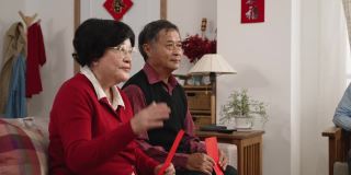 笑容满面的亚洲爷爷和奶奶在中国新年的时候在客厅里向孙女示意要来给她压岁钱。文本翻译:“春天”和“祝贺”