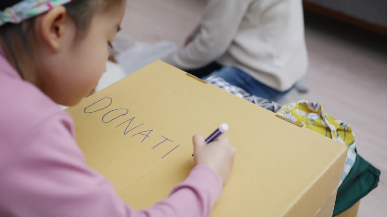 亚洲小孩写和画捐赠的盒子，衣服包装在家里