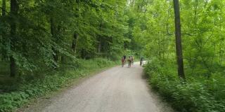 一个带着三个孩子的家庭在穿过绿色森林的碎石路上骑车
