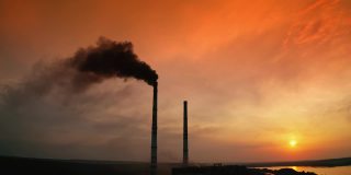 工业管道冒出的黑烟映衬着橙色的天空。日落时河边工厂烟囱的轮廓和黑烟。化学烟雾污染环境。生态灾难。