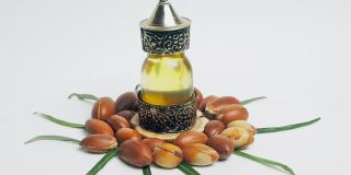 东方玻璃和金属瓶里的摩洛哥坚果油和白色背景上绿色叶子的摩洛哥坚果