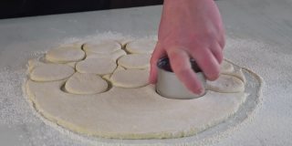一名妇女用圆形模具把生面团切成圆圈，用来做小圆面包、甜甜圈。