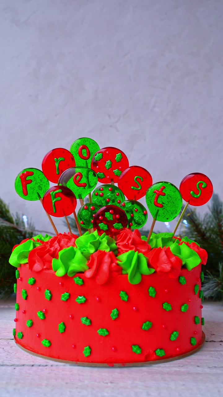 用球装饰圣诞蛋糕，上面刻着“德国节日快乐”的字样。一只女性的手把装饰放在蛋糕上。