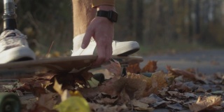 一个戴着金属仿生假肢的年轻人正在秋天的森林里玩滑板。一个假肢在滑板上推着沥青