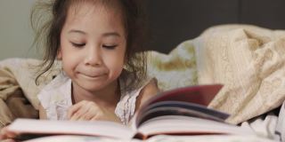 近距离4K的可爱的5岁亚洲女孩，她正在床上看书，美丽的黄色灯光从一盏灯。就寝时间是孩子学习、放松和发展创造力的时间。