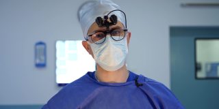 戴眼镜的医生肖像。外科医生戴着双筒放大镜，在手术室对着摄像机讲话。