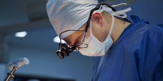 戴口罩的专业医生进行手术。头戴手术灯的外科医生用医疗器械给病人做手术。