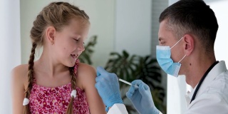 一名戴着医用口罩的医生在一个孩子的肩膀上注射。疫苗接种对冠状病毒。COVID-19疫苗。医生给孩子打了疫苗。一个小女孩在打流感疫苗。