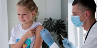 一名戴着医用口罩的医生在一个孩子的肩膀上注射。疫苗接种对冠状病毒。COVID-19疫苗。医生给孩子打了疫苗。一个小女孩在打流感疫苗。