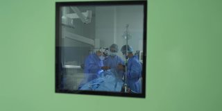 医务人员保健制度。一组穿着防护服的医生为病人做手术。新型冠状病毒肺炎从窗户往外看。