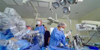 医学新技术。现代临床中的机器人手术。一群穿着医疗制服的医生在医疗机器人旁边给病人做显微手术。
