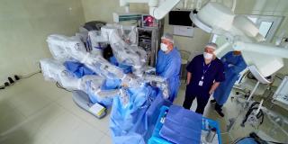 现代手术室中的机器人手术。在微创手术中，一群医疗专家站在机器人旁边。前视图。