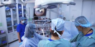 现代手术室的外科手术。身着医疗制服的医生看着屏幕上的手术过程。高科技操作。后视图。