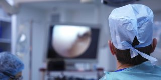 医生们在手术室里使用现代化的医疗设备。外科医生进行手术，并在监视器的屏幕上观察整个过程。后面的观点。
